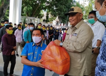 Gubernur Gorontalo, Rusli Habibie (kanan) menyerahkan masker kepada Ketua KNPI Gorontalo, Ghalib Lahidjun, untuk menunjang kegiatan sosialisasi Perda nomor 4 tahun 2020 oleh generasi muda kepada masyarakat Gorontalo, Rabu (28/10/2020). (ari/gopos)