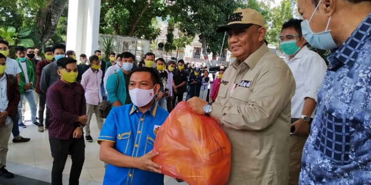 Gubernur Gorontalo, Rusli Habibie (kanan) menyerahkan masker kepada Ketua KNPI Gorontalo, Ghalib Lahidjun, untuk menunjang kegiatan sosialisasi Perda nomor 4 tahun 2020 oleh generasi muda kepada masyarakat Gorontalo, Rabu (28/10/2020). (ari/gopos)