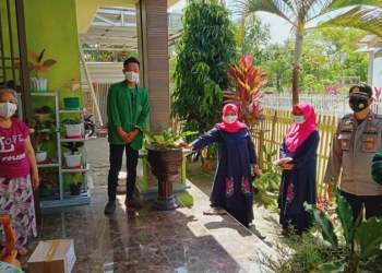 Kapolsek Limboto IPTU Arpaing Ami dibantu beberapa mahasiswa saat memberikan bantuan kepada masyarakat terdampak Covid-19, di Kecamatan Limboto. (Foto: Putra/Gopos)