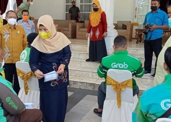 Gubernur Gorontalo Rusli Habibie , didampingi Ketua Tim Penggerak PKK Provinsi Gorontalo, Idah Syahida Rusli Habibie, sedang menyerahkan sembako kepada pengemudi bentor online, secara simbolis. Di Rumah dinas gubernur, Kamis (8/7/2021). (Foto: Sari/gopos)