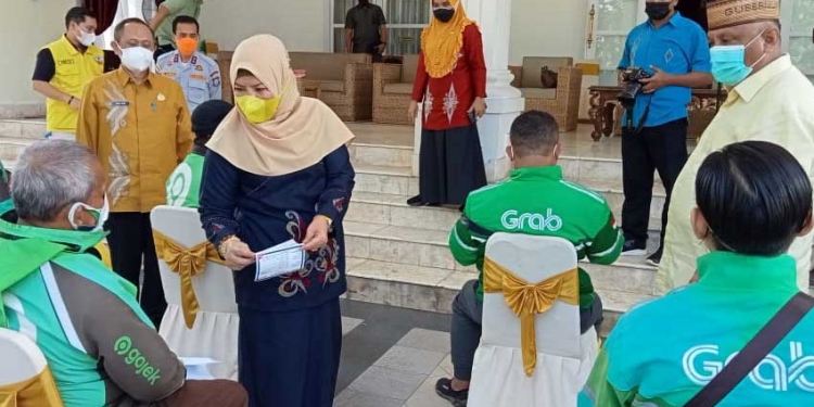 Gubernur Gorontalo Rusli Habibie , didampingi Ketua Tim Penggerak PKK Provinsi Gorontalo, Idah Syahida Rusli Habibie, sedang menyerahkan sembako kepada pengemudi bentor online, secara simbolis. Di Rumah dinas gubernur, Kamis (8/7/2021). (Foto: Sari/gopos)