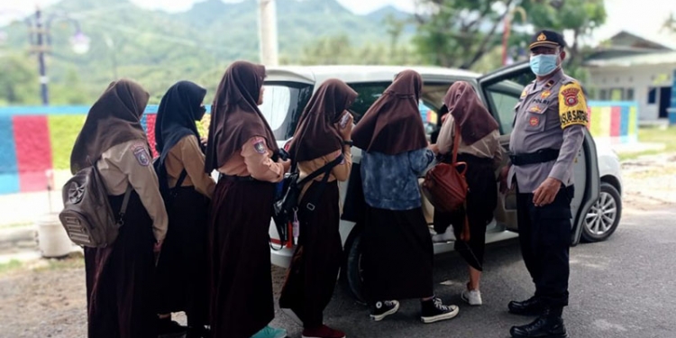 Kapolsek Bone Raya, Ipda Gendut Hartono, mengantar jemput pelajar untuk memudahkan mereka mengikuti vaksinasi, Jumat (22/10/2021). (Dok. Polda Gorontalo)