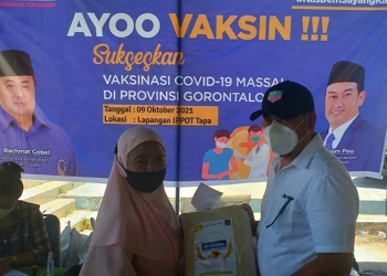 Ketua DPW Partai Nasdem Provinsi Gorontalo, Hamim Pou saat menyerahkan hadiah kegembiraan berupa beras Premium Amazinc kepada warga yang telah melakukan vaksinasi. (Foto Indra/Gopos)