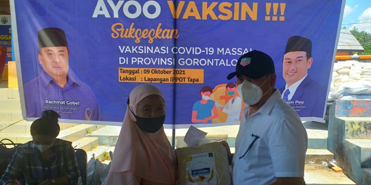 Ketua DPW Partai Nasdem Provinsi Gorontalo, Hamim Pou saat menyerahkan hadiah kegembiraan berupa beras Premium Amazinc kepada warga yang telah melakukan vaksinasi. (Foto Indra/Gopos)
