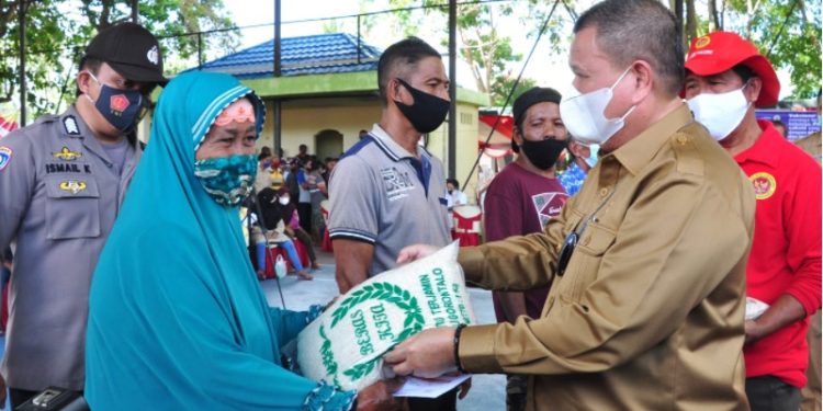 Idris Rahim (kanan), menyerahkan bantuan beras kepada warga yang mengikuti vaksinasi massal yang digelar oleh Binda Provinsi Gorontalo di Kecamatan Tilamuta, Kabupaten Boalemo. (Foto: Haris)