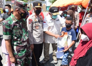 Gubernur Gorontalo Rusli Habibie, didampingi Danrem 133 NWB, Kapolda Gorontalo, saat menyerahkan bantuan beras kepada salah seorang warga masyarakat Kabupaten Gorontalo, usai menerima vaksinasi di depan Masjid Baitulrahman Limboto, Kabupaten Gorontalo, Sabtu (11/12/2021). (Foto – Salman)