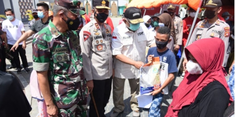 Gubernur Gorontalo Rusli Habibie, didampingi Danrem 133 NWB, Kapolda Gorontalo, saat menyerahkan bantuan beras kepada salah seorang warga masyarakat Kabupaten Gorontalo, usai menerima vaksinasi di depan Masjid Baitulrahman Limboto, Kabupaten Gorontalo, Sabtu (11/12/2021). (Foto – Salman)