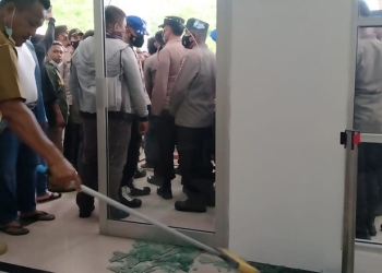 Staf Deprov Gorontalo membersihkan material kaca dari pintu depan yang pecah dalam aksi demonstrasi tentang tambang rakyat di Deprov Gorontalo, Senin (14/3/2022). (muhajir/gopos)