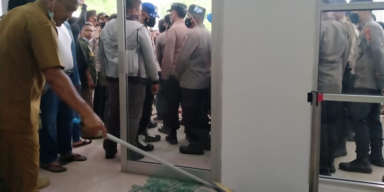 Staf Deprov Gorontalo membersihkan material kaca dari pintu depan yang pecah dalam aksi demonstrasi tentang tambang rakyat di Deprov Gorontalo, Senin (14/3/2022). (muhajir/gopos)