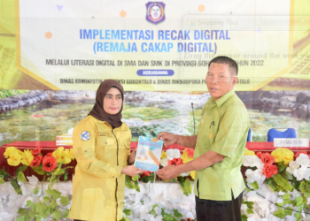 Kepala Bidang Informasi Komunikasi Publik (IKP) Diskominfotik Provinsi Gorontalo, Zakiya Baserewan (kiri), menyerahkan manual book Panduan Remaja Cakap Digital kepada Wakil Kepala Sekolah SMA 1 Marisa, I Nyoman Sarda, pada kegiatan Implementasi Recak Digital, di aula SMA 1 Marisa, Kamis (19/5/22). ( Foto: Alfred)