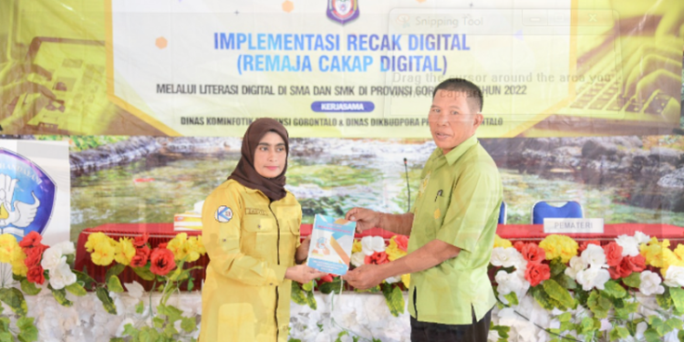 Kepala Bidang Informasi Komunikasi Publik (IKP) Diskominfotik Provinsi Gorontalo, Zakiya Baserewan (kiri), menyerahkan manual book Panduan Remaja Cakap Digital kepada Wakil Kepala Sekolah SMA 1 Marisa, I Nyoman Sarda, pada kegiatan Implementasi Recak Digital, di aula SMA 1 Marisa, Kamis (19/5/22). ( Foto: Alfred)