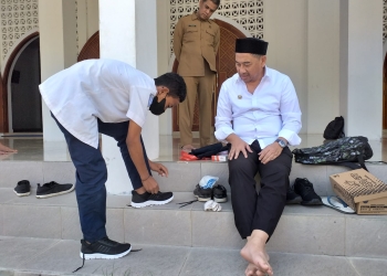 Bupati Hamim, Bupati Hamim Pou saat menyerahkan sepatu baru dan peralatan sekolah lainnya kepada Abdul Muzil Usuli sekaligus mengenakannya kepada siswa yang duduk di bangku SMP Negeri 3 Suwawa kelas VII itu, usai salat dzuhur di Masjid Agung Baitul Haq Islamic Center, Senin (6/6/2022). (Foto Indra/Gopos)
