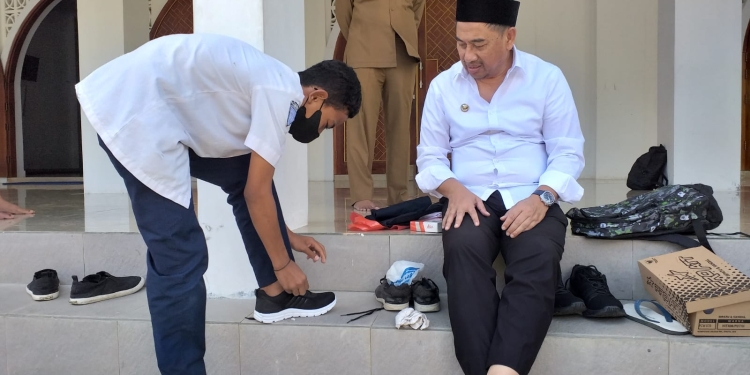 Bupati Hamim, Bupati Hamim Pou saat menyerahkan sepatu baru dan peralatan sekolah lainnya kepada Abdul Muzil Usuli sekaligus mengenakannya kepada siswa yang duduk di bangku SMP Negeri 3 Suwawa kelas VII itu, usai salat dzuhur di Masjid Agung Baitul Haq Islamic Center, Senin (6/6/2022). (Foto Indra/Gopos)