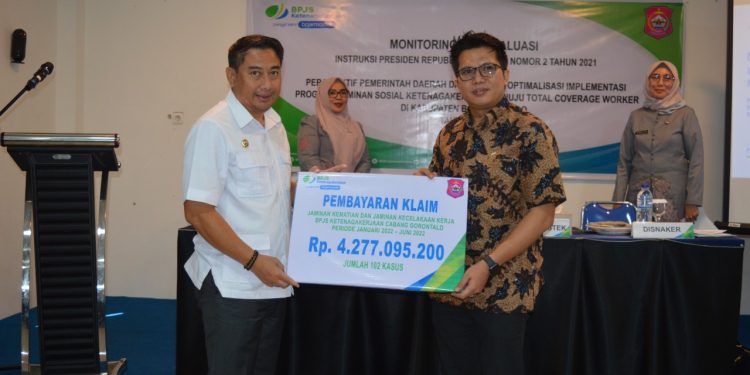 Kepala BPJamsostek Cabang Gorontalo, Hendra Elvian, menyerahkan pembayaran klaim kepesertaan, baik JKK dan JKM periode Januari 2022 – Juni 2022 sebesar Rp4,2 miliar lebih dengan 102 kasus kepada Bupati Bone Bolango Hamim Pou, pada kegiatan Monitoring dan Evaluasi Instruksi Presiden Nomor 2 Tahun 2021 di Hotel Toewawa, Kamis (23/6/2022). (Foto AKP/Diskominfo)