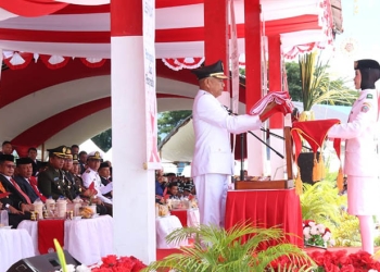 Bupati Pohuwato, Saipul  Mbuinga, saat menyerahkan bendera merah putih kepada pembawa baki dalam upacara pengibaran bendera merah putih, hari ulang tahun (HUT) ke-77 RI, di lapangan Proklamasi, Kecamatan Popayato, Rabu 17/08/2022 (Istimewa )