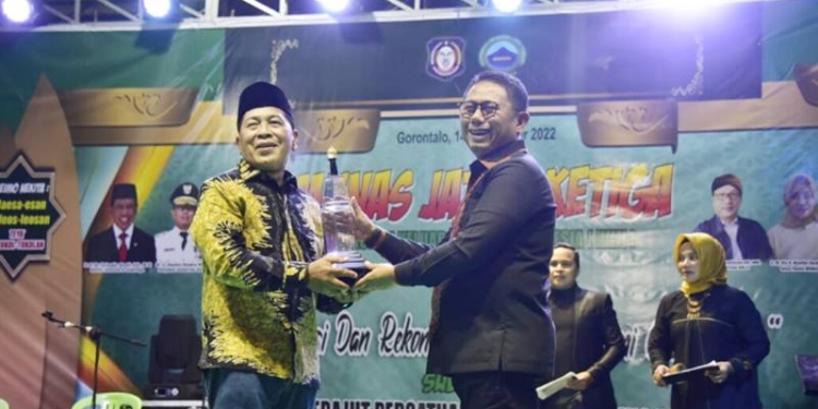 Penyerahan piala bergilir festival budaya Jaton ke 16 dari Kontingen dari Tondano, Sulawesi Utara diserahkan kepada Penjagub Hamka Hendra Noer, saat pembukaan Musyawarah Nasional Kerukunan Keluarga Jaton Indonesia (KKJI) ke-tiga yang dilaksanakan di Kampung Jawa Yosonegoro, Kecamatan Limboto, Kabupaten Gorontalo, Jumat malam (14/10/2022). Foto – Nova