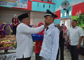 : Bupati Bone Bolango, Hamim Pou saat memasang tanda jabatan kepada Kepala Desa Poduwoma, Agus Salim Ishak, Sabtu (21/1/2023). (Foto Indra/Gopos)