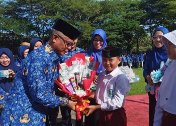 Sekda Ishak Ntoma saat menyerahkan Kartu Identitas Anak (KIA) dan Bucket Snack Ringan kepada perwakilan siswa Sekolah Dasar saat pelaksanaan Apel Korpri di lingkungan Pemerintah Kabupaten Bone Bolango di Halaman Kantor Bupati, Jumat (17/2/2023). (Foto AKP/Diskominfo)