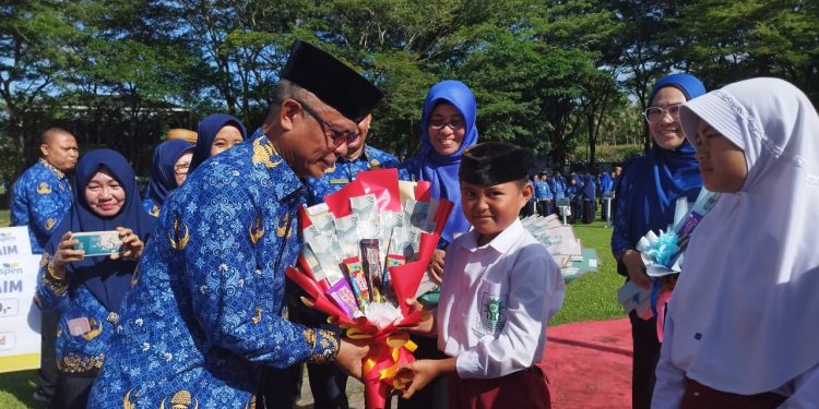 Sekda Ishak Ntoma saat menyerahkan Kartu Identitas Anak (KIA) dan Bucket Snack Ringan kepada perwakilan siswa Sekolah Dasar saat pelaksanaan Apel Korpri di lingkungan Pemerintah Kabupaten Bone Bolango di Halaman Kantor Bupati, Jumat (17/2/2023). (Foto AKP/Diskominfo)