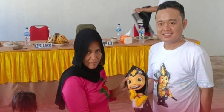Anggota KPU Gorut Noval Katili menyerahkan boneka maskot Pilkada kepada warga Anggrek setelah kegiatan sosialisasi, Senin (28/10/2024).