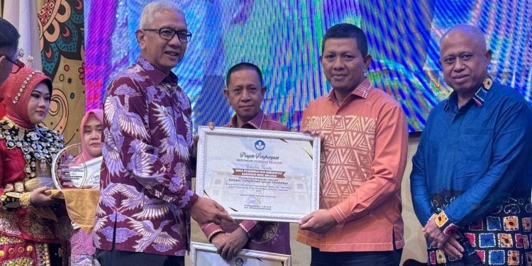 Penjabat Gubernur Gorontalo, Rudy Salahuddin saat menyerahkan Piagam Penghargaan kebijakan Merdeka Belajar kepada Kepala Dinas Pendidikan dan Kebudayaan Kabupaten Bone Bolango, Adrien Andjar di Hotel Aston Kota Gorontalo, Minggu (20/10/2024). (Foto Istimewa)