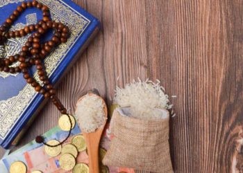 Coins, rosary, Holy Quran and rice in the sack. Zakat concept. Zakat is a form of alm-giving as a religious obligation or tax. Large Arab word right method to read correctly.