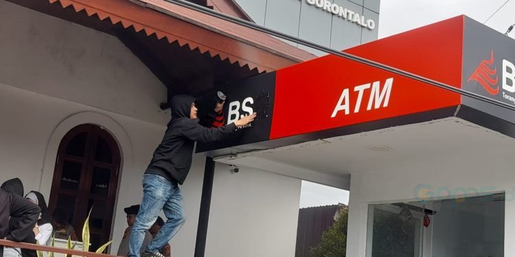 Salah satu massa aksi menutup huruf G yang ada ATM Kantor BSG Wilayah Gorontalo sebagai aksi protes. (foto.isno/gopos)
