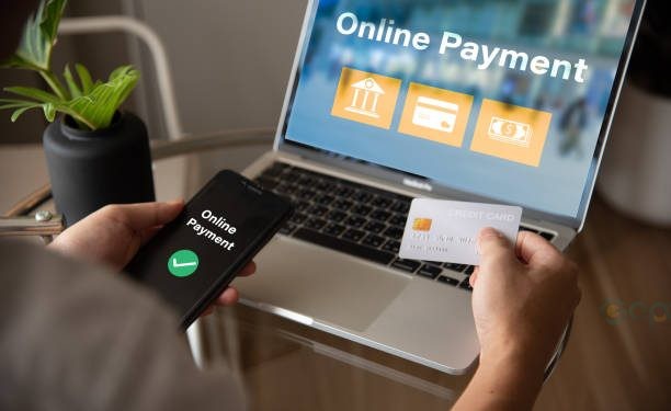 A person is using a laptop to pay for something online. They are holding a credit card and a phone
