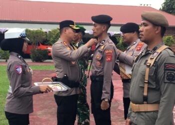 Kapolres Bone Bolango, AKBP Supriantoro saat menyematkan pita merah kepada perwakilan personel yang terlibat dalam Operasi Kepolisian Terpusat Lilin Otanaha 2025 dalam rangka Pelayanan Perayaan Natal 2025 dan Tahun Baru 2026 di Halaman Mapolres Bone Bolango, Jumat (19/12/2025). (Foto Indra/Gopos)