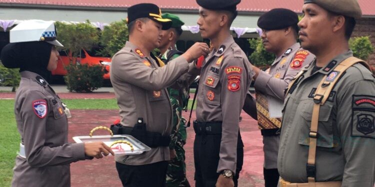 Kapolres Bone Bolango, AKBP Supriantoro saat menyematkan pita merah kepada perwakilan personel yang terlibat dalam Operasi Kepolisian Terpusat Lilin Otanaha 2025 dalam rangka Pelayanan Perayaan Natal 2025 dan Tahun Baru 2026 di Halaman Mapolres Bone Bolango, Jumat (19/12/2025). (Foto Indra/Gopos)