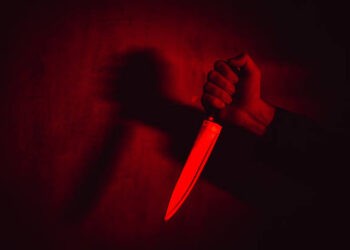 Close-up of a man holding a knife under neon lights.