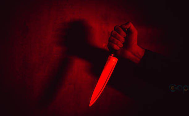 Close-up of a man holding a knife under neon lights.