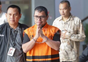 Bupati Bolaang Mongondow Utara, Sirajudin Lasena (tengah) mengenakan rompi tahanan berjalan menuju mobil tahanan usai menjalani pemeriksaan di Gedung Merah Putih KPK, Jakarta, Selasa (22/9/2026). [Suara.com]