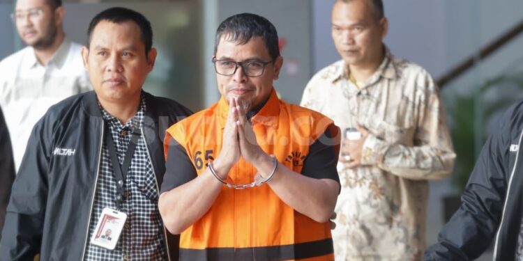 Bupati Bolaang Mongondow Utara, Sirajudin Lasena (tengah) mengenakan rompi tahanan berjalan menuju mobil tahanan usai menjalani pemeriksaan di Gedung Merah Putih KPK, Jakarta, Selasa (22/9/2026). [Suara.com]