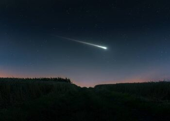 Fireball in the evening sky over the fields. Bright shooting star. Meteor illuminates the starry sky. (Ilustrasi)